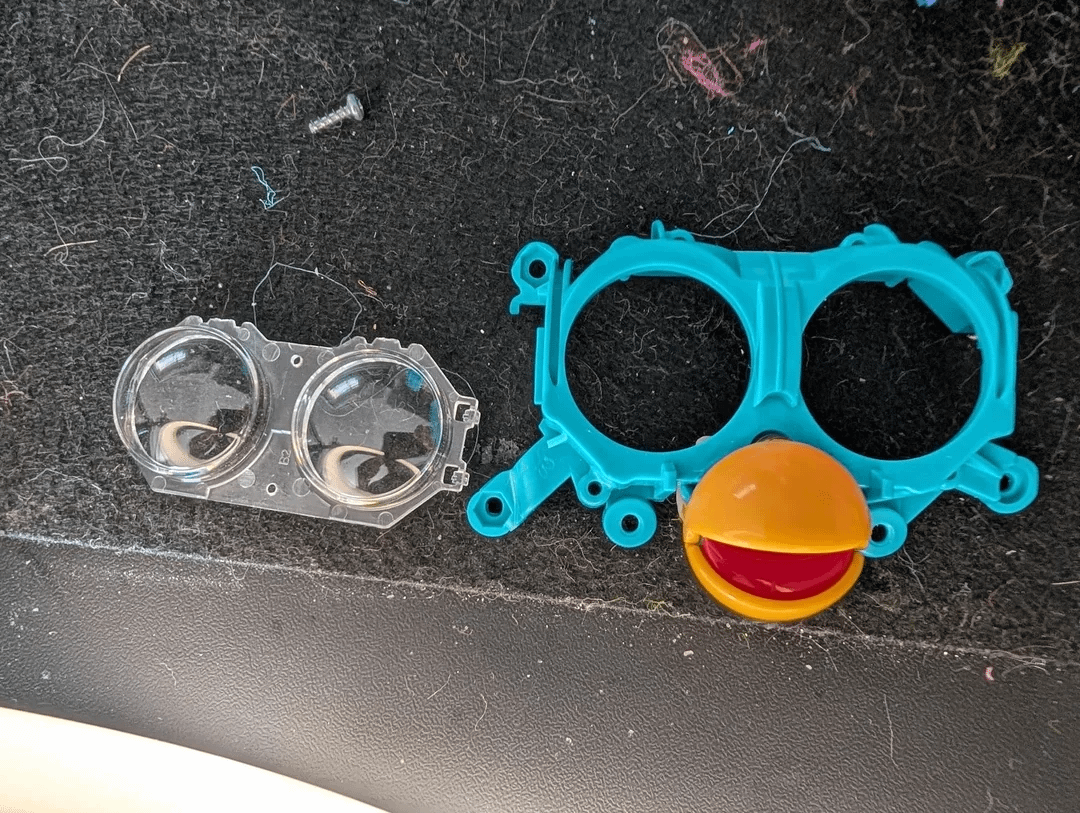 Clear plastic Furby eye cover removed from the holder